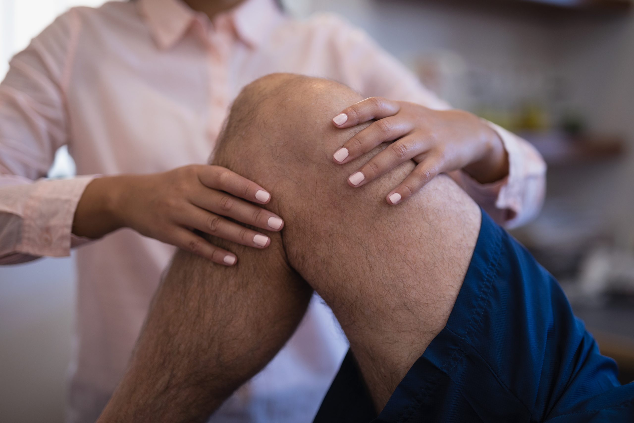 Midsection of female therapist examining knee with senior male patient at hospital ward